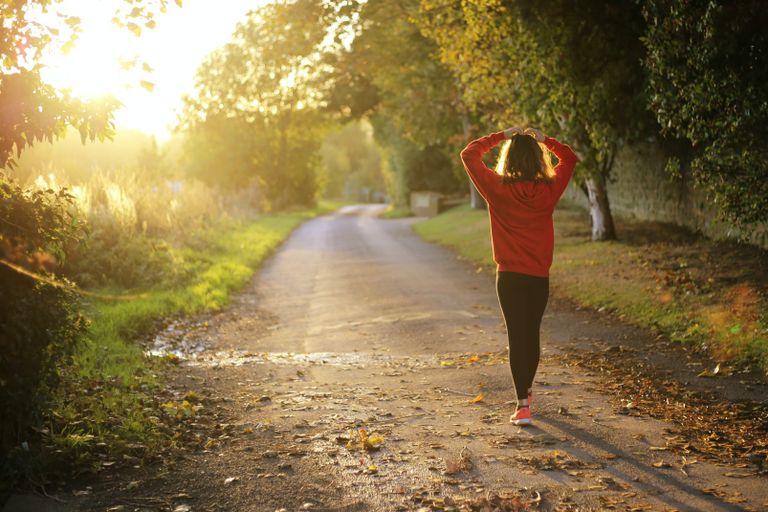 Woman walking along a road with her hands placed on her head, practicing balance