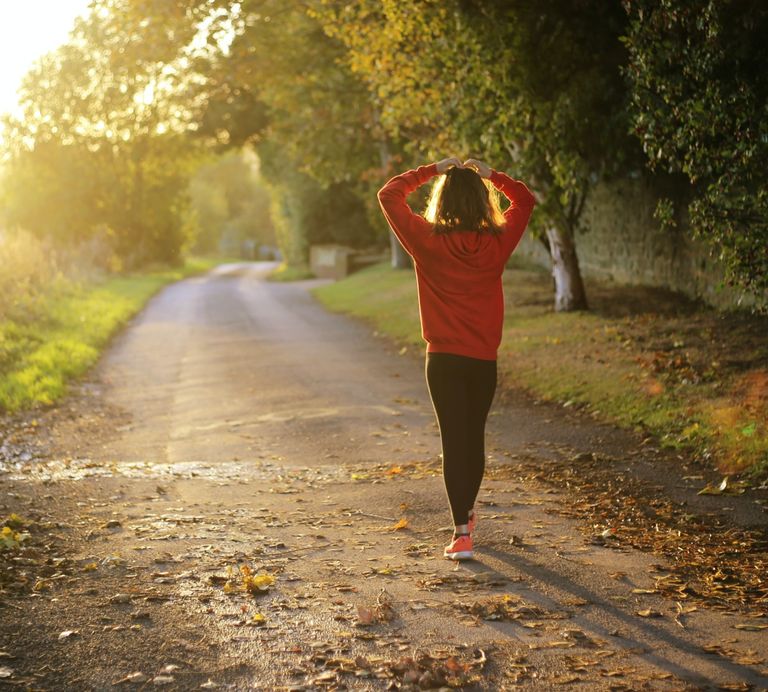 Woman walking along a road with her hands placed on her head, practicing balance
