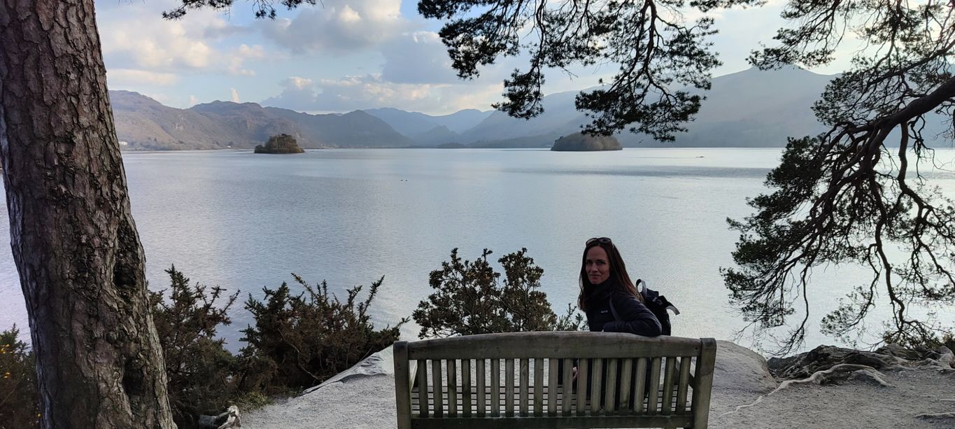 Sarah Lord sat on a bench in Keswick with Derwent Water in the background